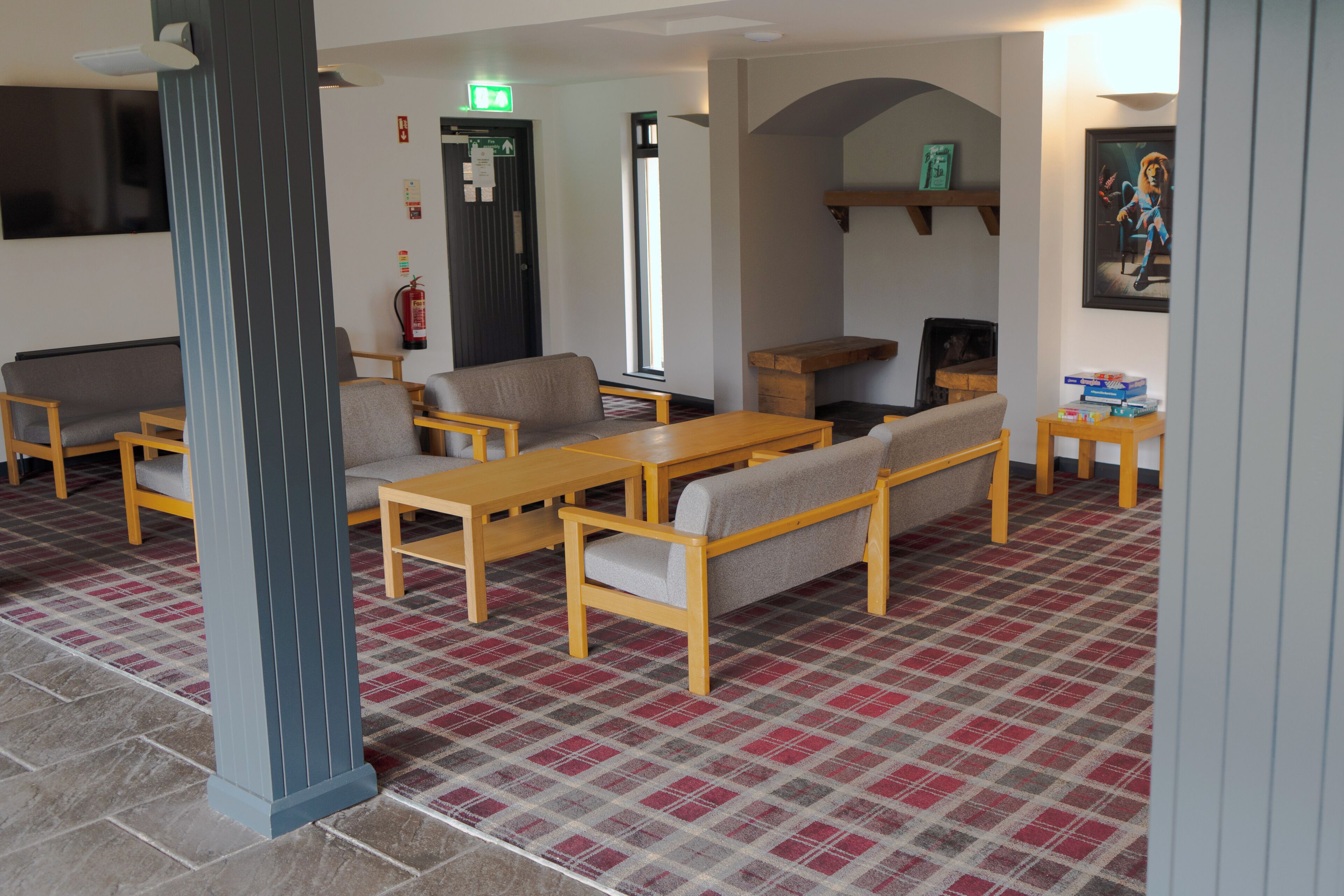 A lobby with a checkered floor, wooden furniture, a fire extinguisher, and a framed picture on the wall.