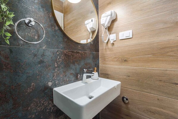 A bathroom with a white sink, a round mirror, and a hairdryer mounted on the wall.