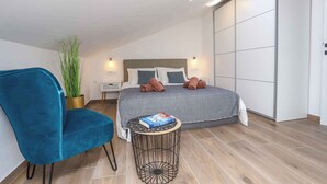 A modern bedroom with a bed, a blue chair, a small round table, and a potted plant.