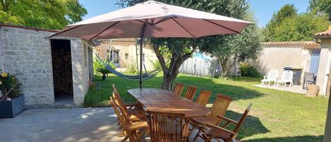 A patio with a wooden table and chairs, a large umbrella, and a hammock.