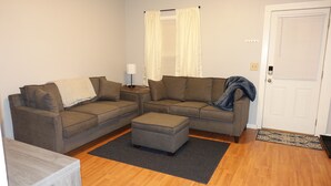 A living room with two sofas, a coffee table, a lamp, and a door with a doormat. - The College Cottage - Entire Home (Morehead)