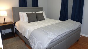 A neatly made bed with a grey upholstered headboard, a bedside table with a lamp, and a grey rug. - The College Cottage - Entire Home (Morehead)