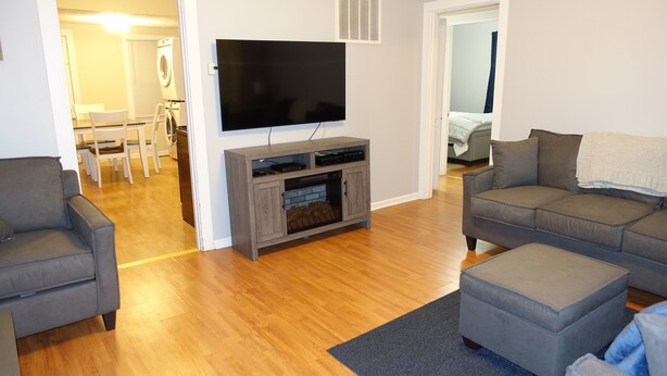 A living room with a flat-screen TV, grey sofas, and a wooden floor. - The College Cottage - Entire Home (Morehead)