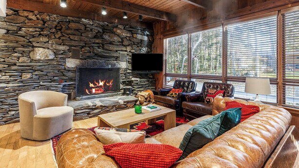 A cozy living room with a stone fireplace, comfortable seating, and large windows.