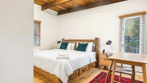 A bedroom with a wooden bed, white bedding, a wooden table, and a red rug.