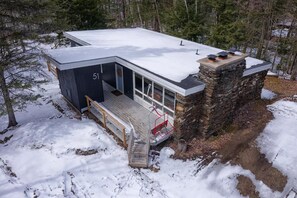 Enjoy the serene winter landscape from the comfort of this cabin's spacious interior, featuring a prominent chimney and a large roof.