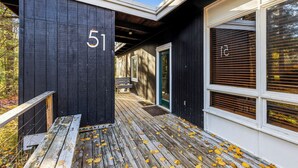 A wooden deck with a bench, a black building with the number 51, and a window with blinds.