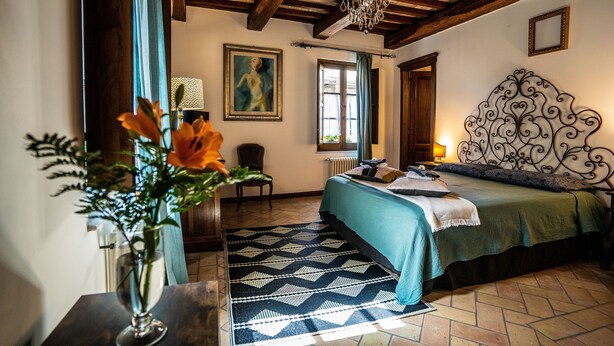 Une chambre à coucher avec un lit, une chaise, un tableau, un lustre et une fenêtre.