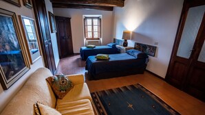 Une pièce confortable avec un canapé, deux lits avec une literie bleue, un tapis à motifs et une fenêtre avec des volets.