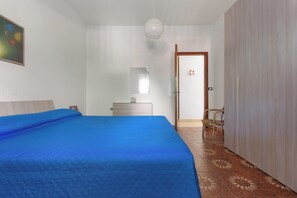 Un dormitorio con cama, mesita de noche, cómoda, espejo, puerta y silla.