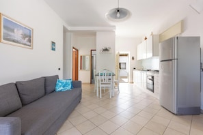 Una sala moderna con un sofá gris, una mesa de comedor y una cocina con refrigerador.