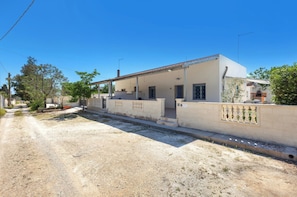 Une maison à deux étages avec un porche abrité, un petit jardin et un chemin de terre.