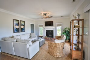 A living room with a sectional sofa, a fireplace, a ceiling fan, and a bookshelf.