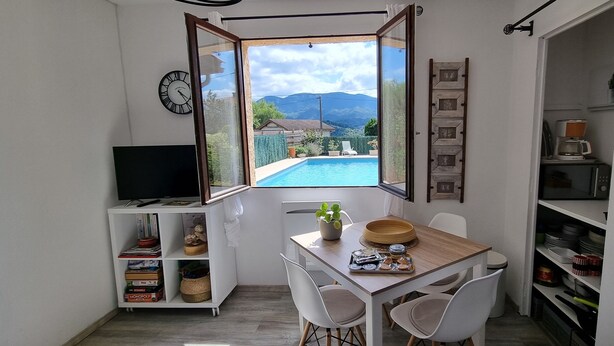Cocina compacta con comedor, televisor y vista a una piscina y montañas.