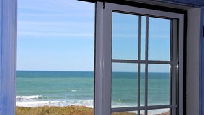 Une vue sur l’océan, prise à travers une fenêtre, avec un ciel dégagé et une zone herbeuse au premier plan.