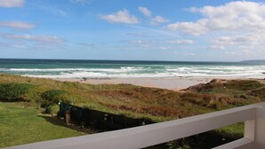 Une vue côtière avec un premier plan herbeux, une plage de sable et l’océan sous un ciel partiellement nuageux.