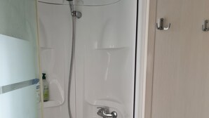 A walk-in shower with a handheld showerhead, a built-in seat, and a small shelf. - Mobile home rental (Mimizan)