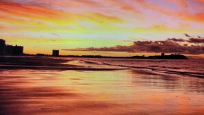 Ein Sonnenuntergang über einem Strand mit einer fernen Küstenlinie und einer Bausubstanz.