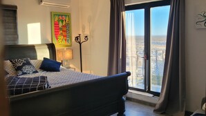Ein Schlafzimmer mit einem großen Bett, einem Deckenventilator, einem Fenster mit Vorhängen und Blick auf die Stadt.