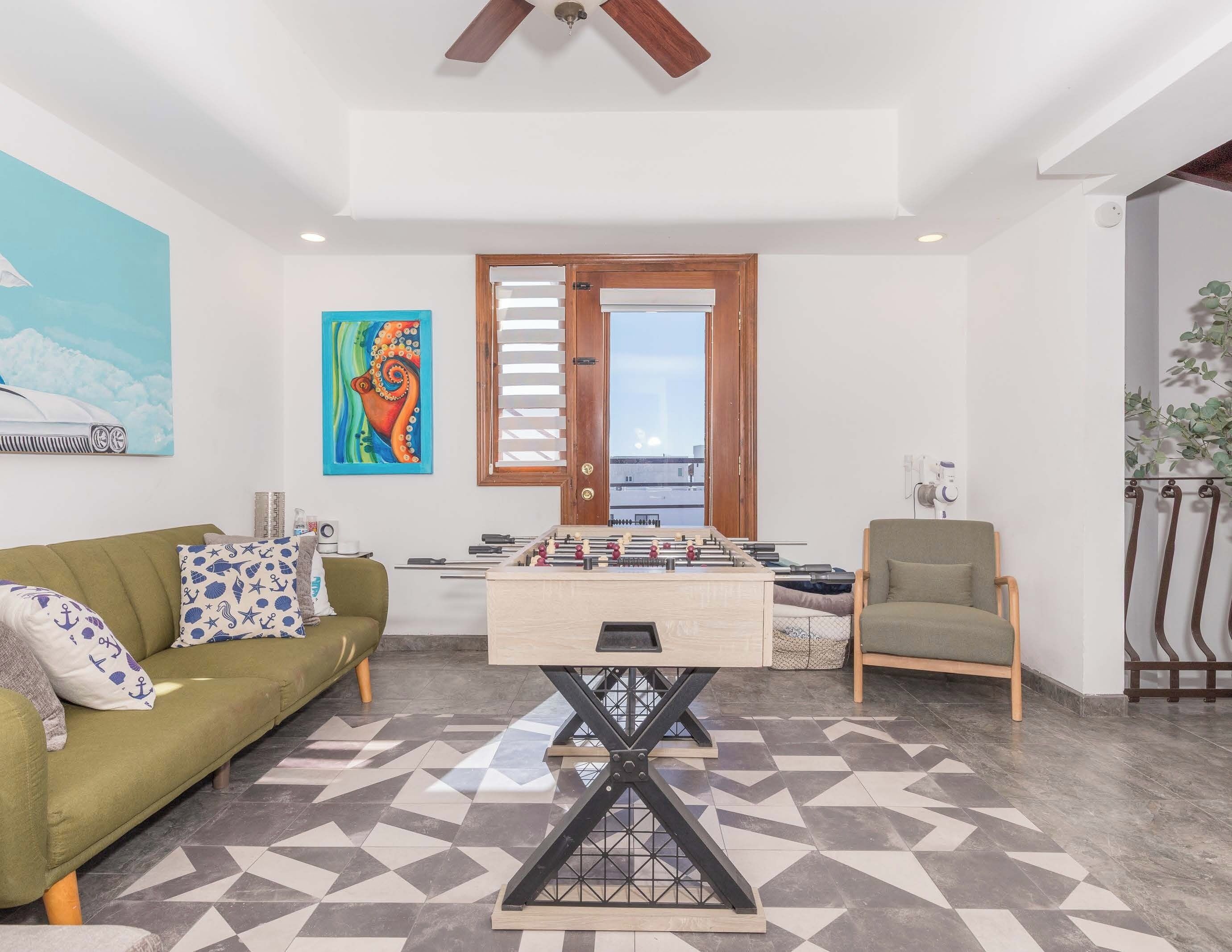 A living room with a foosball table, a sofa, a chair, and a painting on the wall.