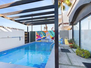 A swimming pool with a pergola overhead, surrounded by a white wall and a colorful mural.