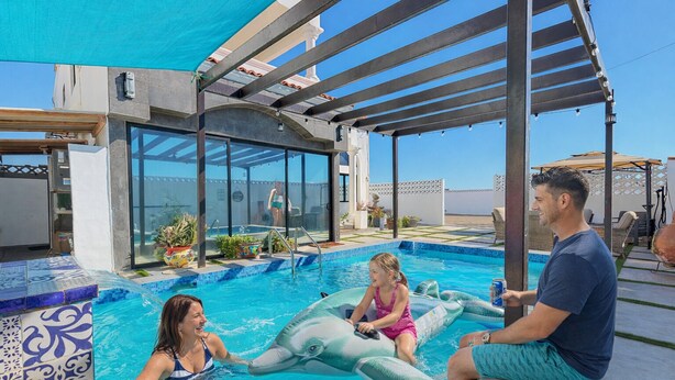 Ein Schwimmbad mit Glasverkleidung, einem überdachten Sitzbereich und Blick auf das Meer.