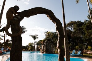 Un espace piscine agrémenté d’une structure en pierre, de palmiers et de chaises longues.