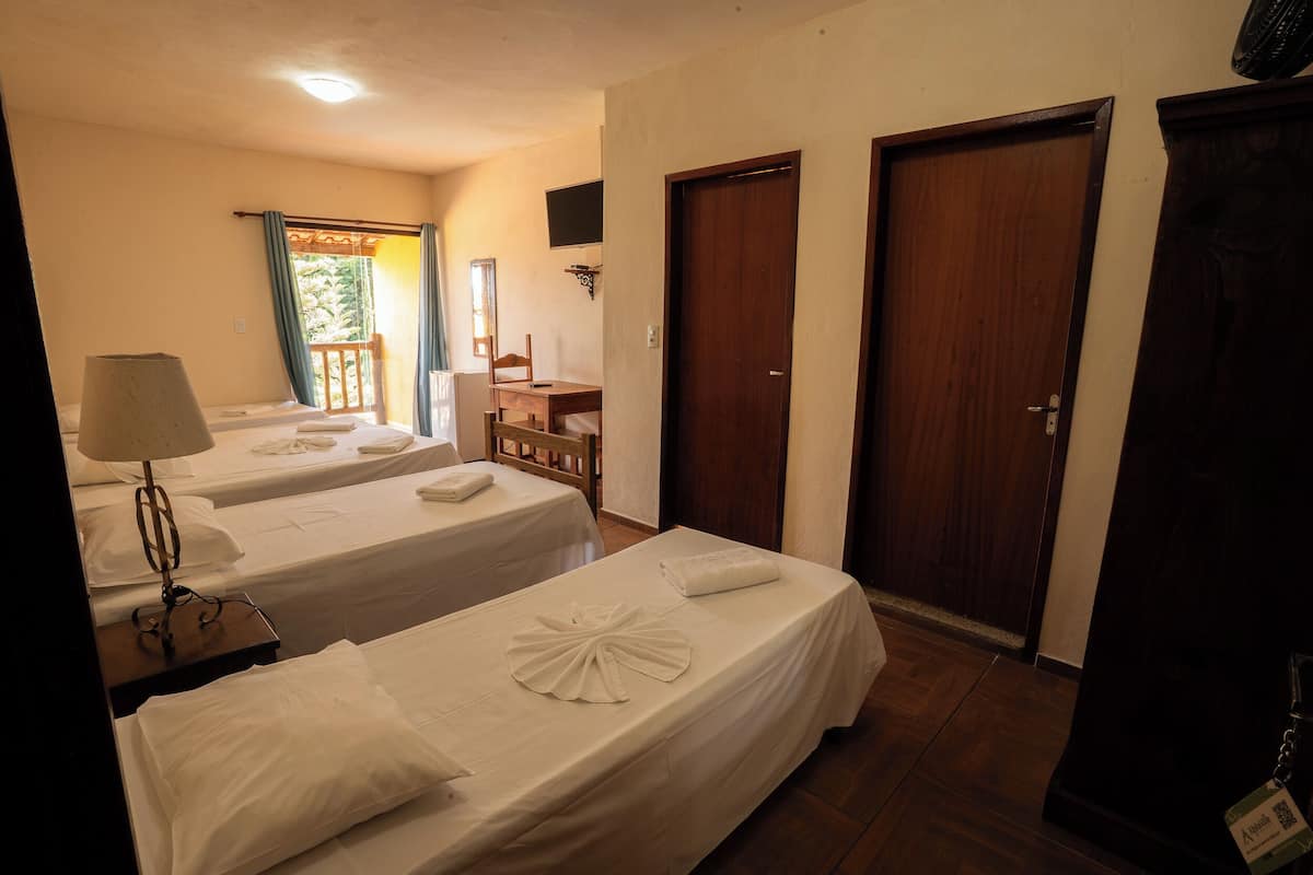 Quarto de hotel com duas camas, uma escrivaninha, uma cadeira, uma televisão e um guarda-roupa.
