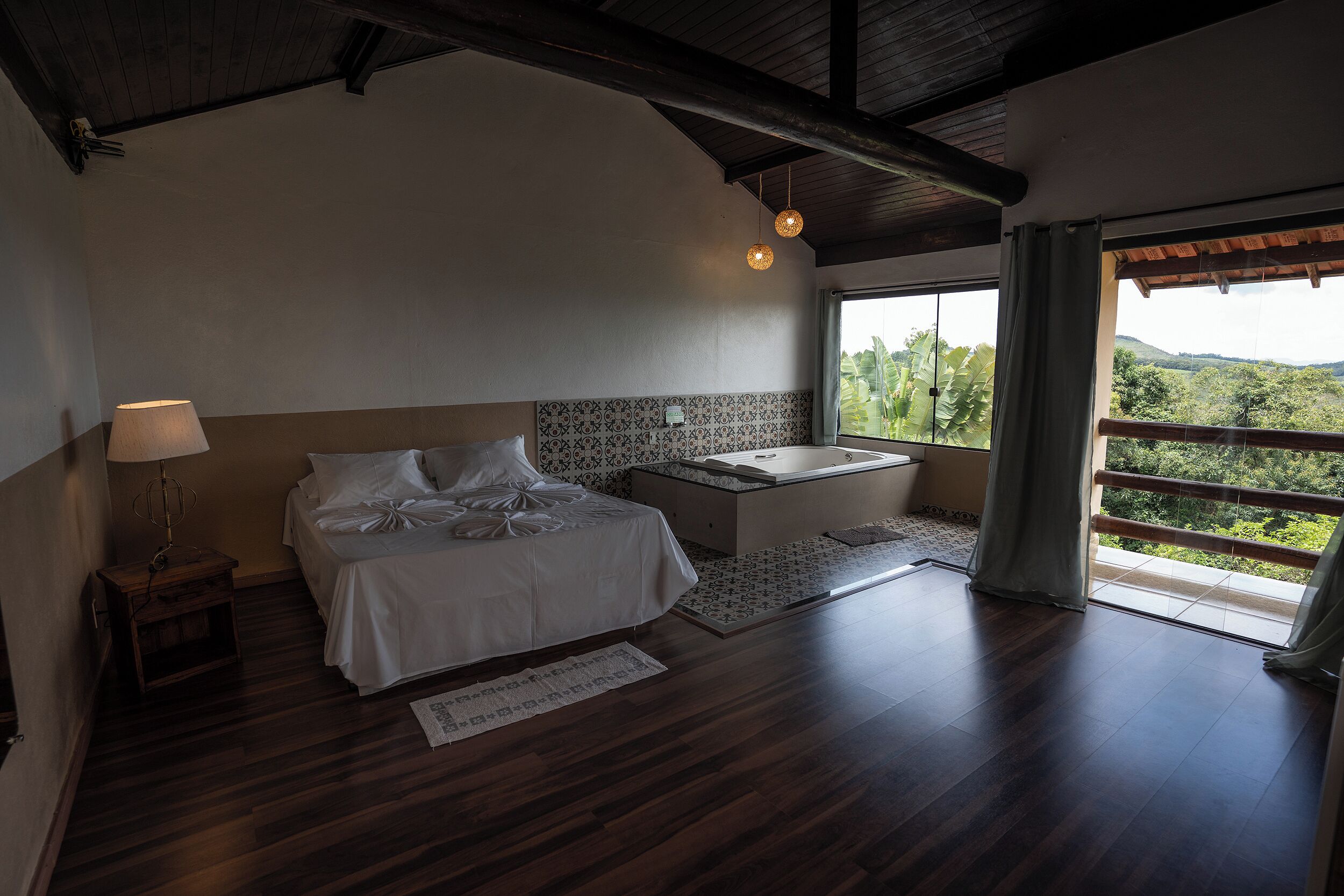 Un dormitorio con cama, mesita de noche, lámpara y vistas al exterior.