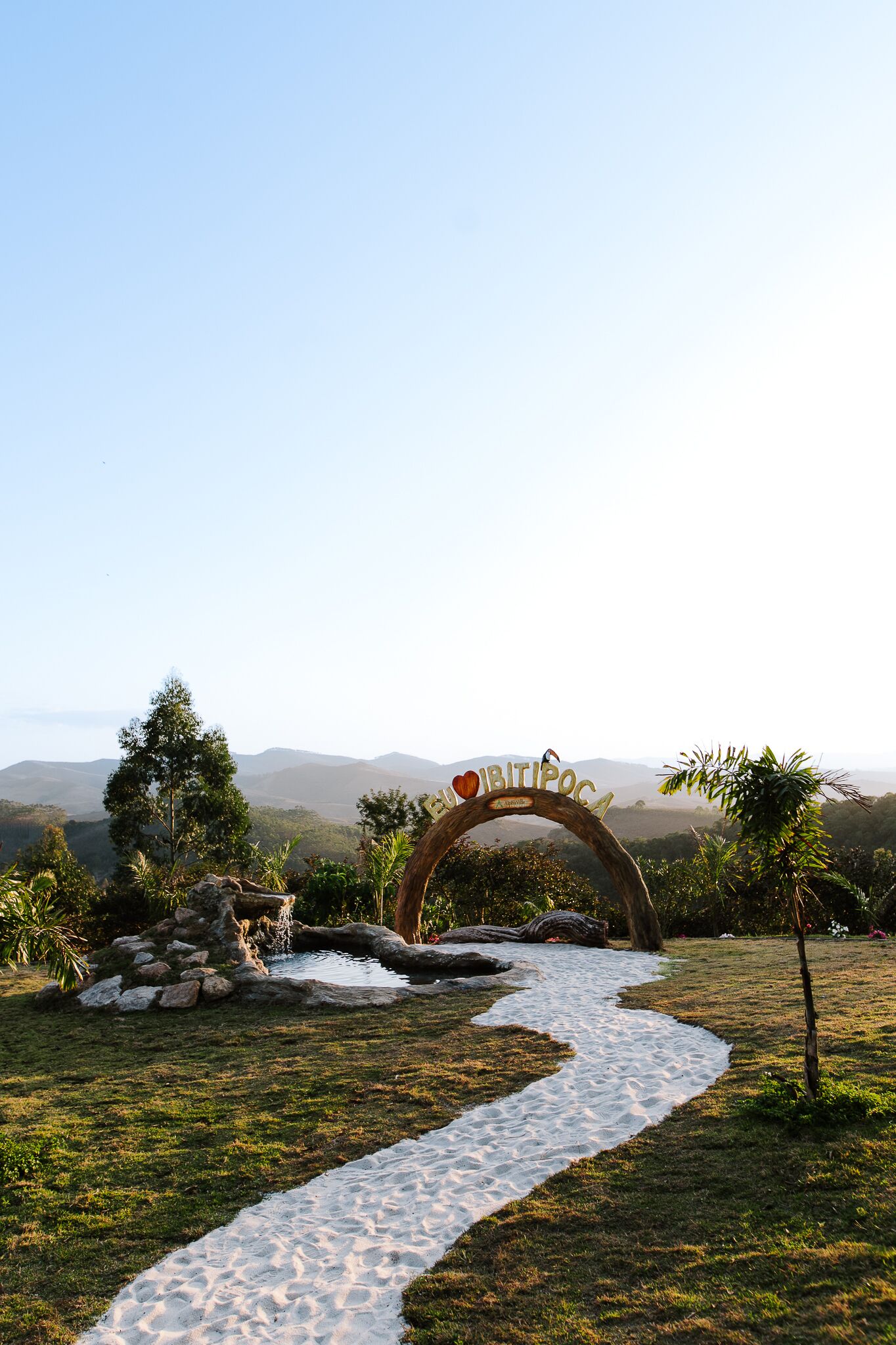 A pathway leading to a wooden archway with the inscription "BITIPOSA" and a heart symbol.