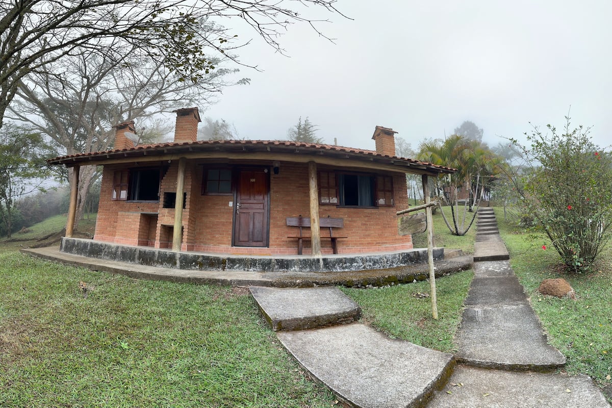Uma casa rústica de tijolos com varanda, porta de madeira e chaminé.