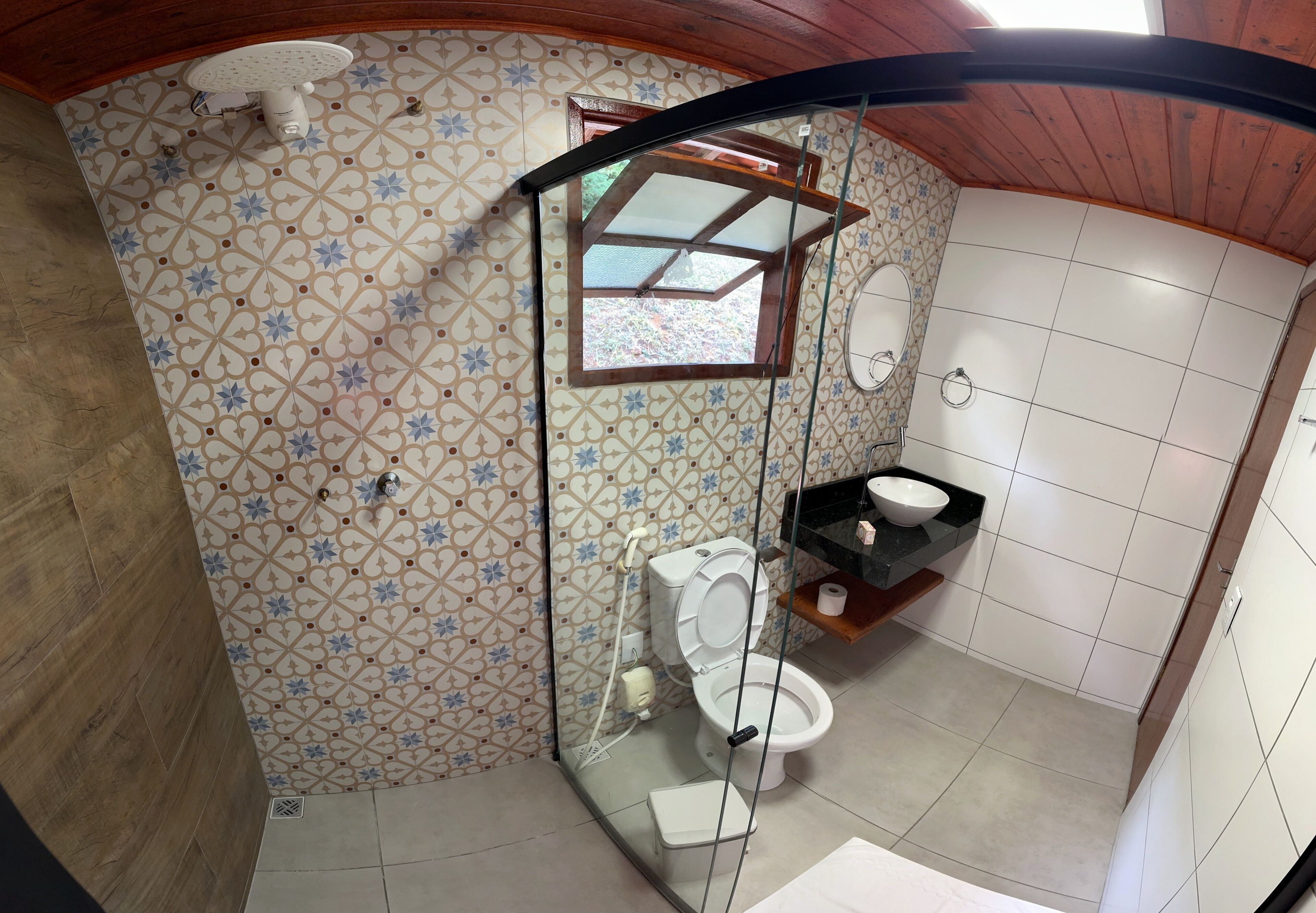 A bathroom with a patterned tile wall, a toilet, a glass-enclosed shower, and a sink with a black countertop.