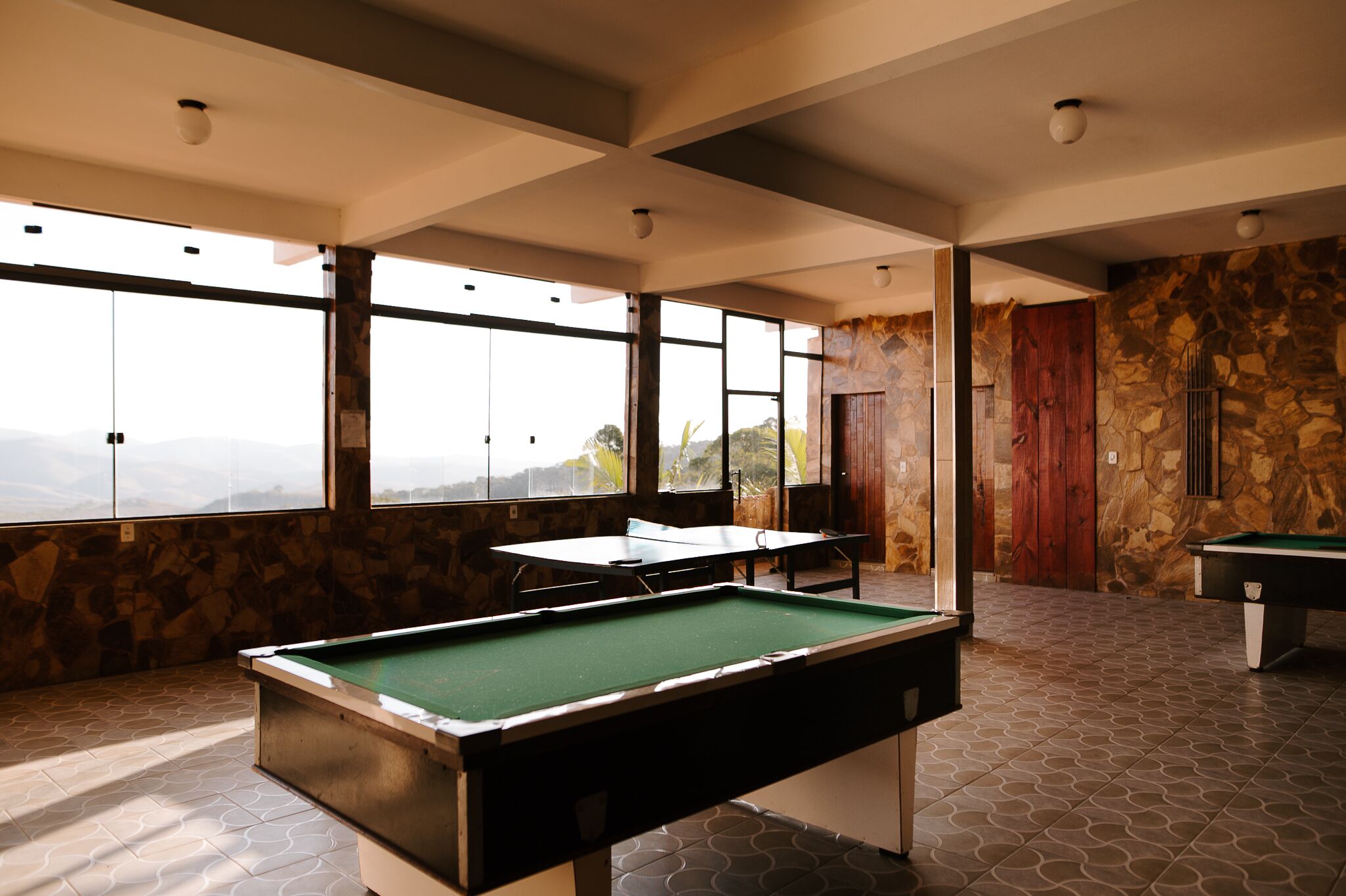 A pool table in a room with large windows, stone walls, and a view of the mountains.