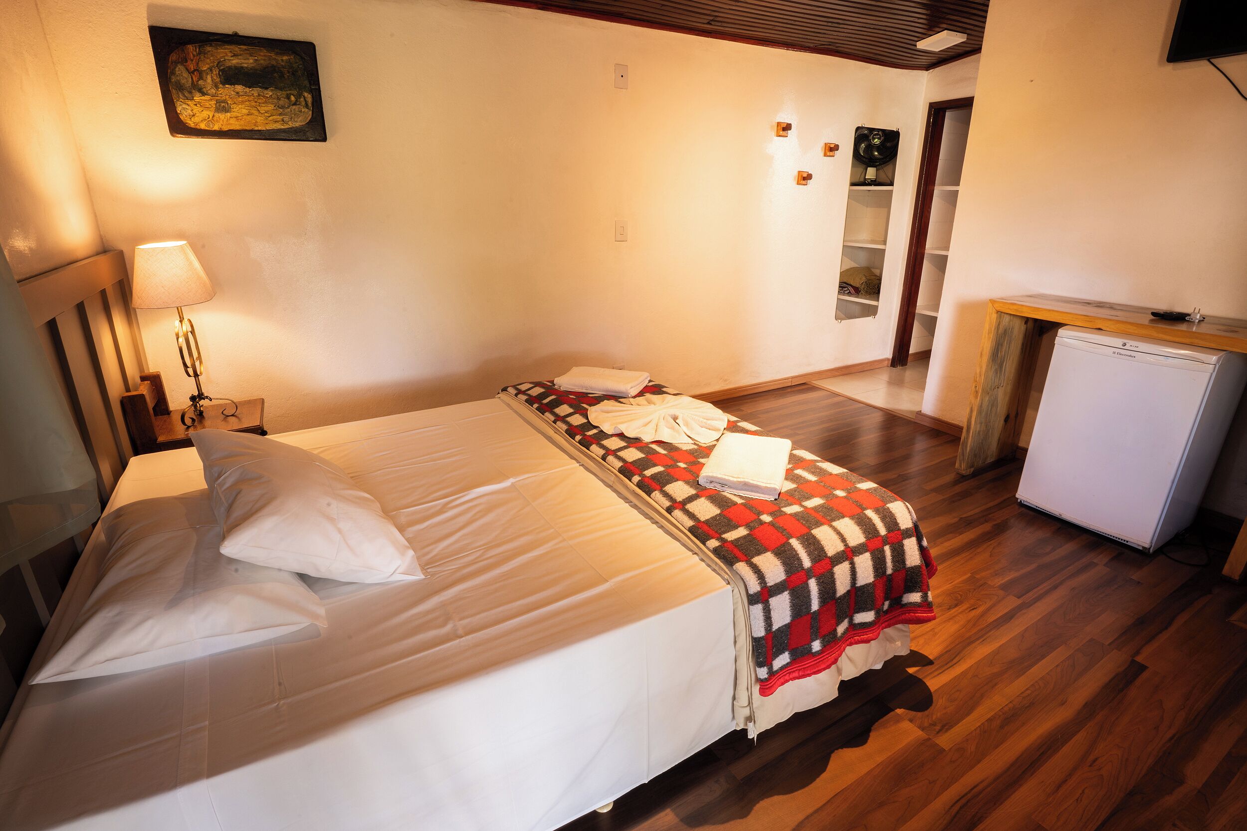 A room with a bed, a desk, a lamp, and a refrigerator.