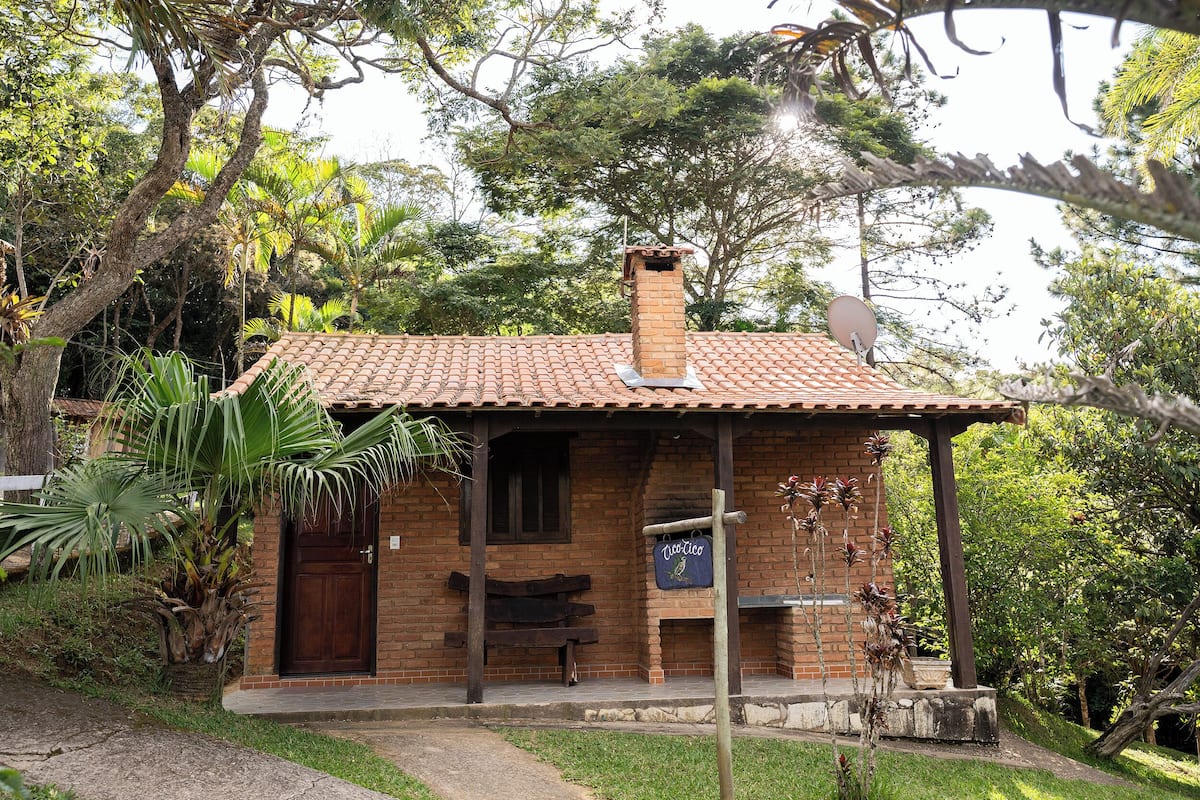 Uma pequena casa de tijolos com telhado de cerâmica, porta de madeira e um banco na frente.