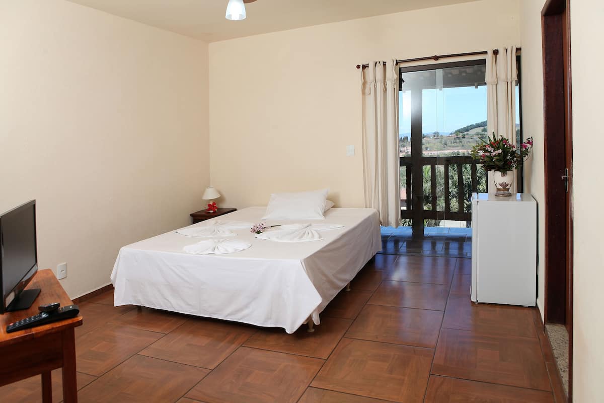 Quarto de hotel com cama, televisão, escrivaninha e varanda com vista.