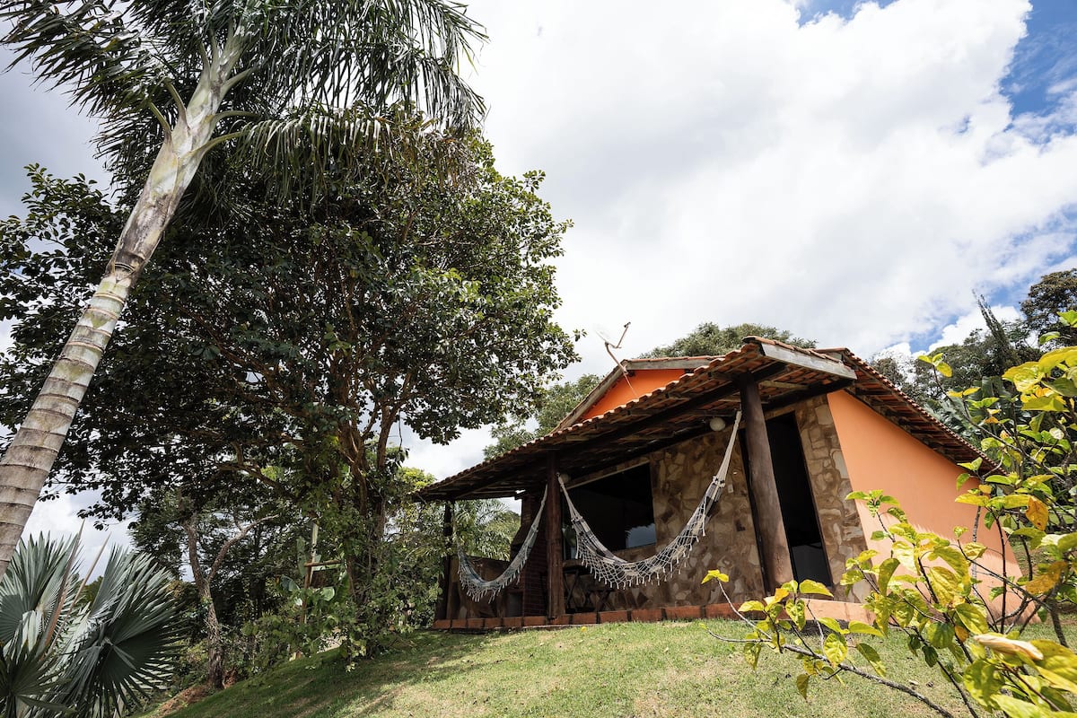 Um edifício rústico com fachada de pedra, varanda de madeira e uma rede.