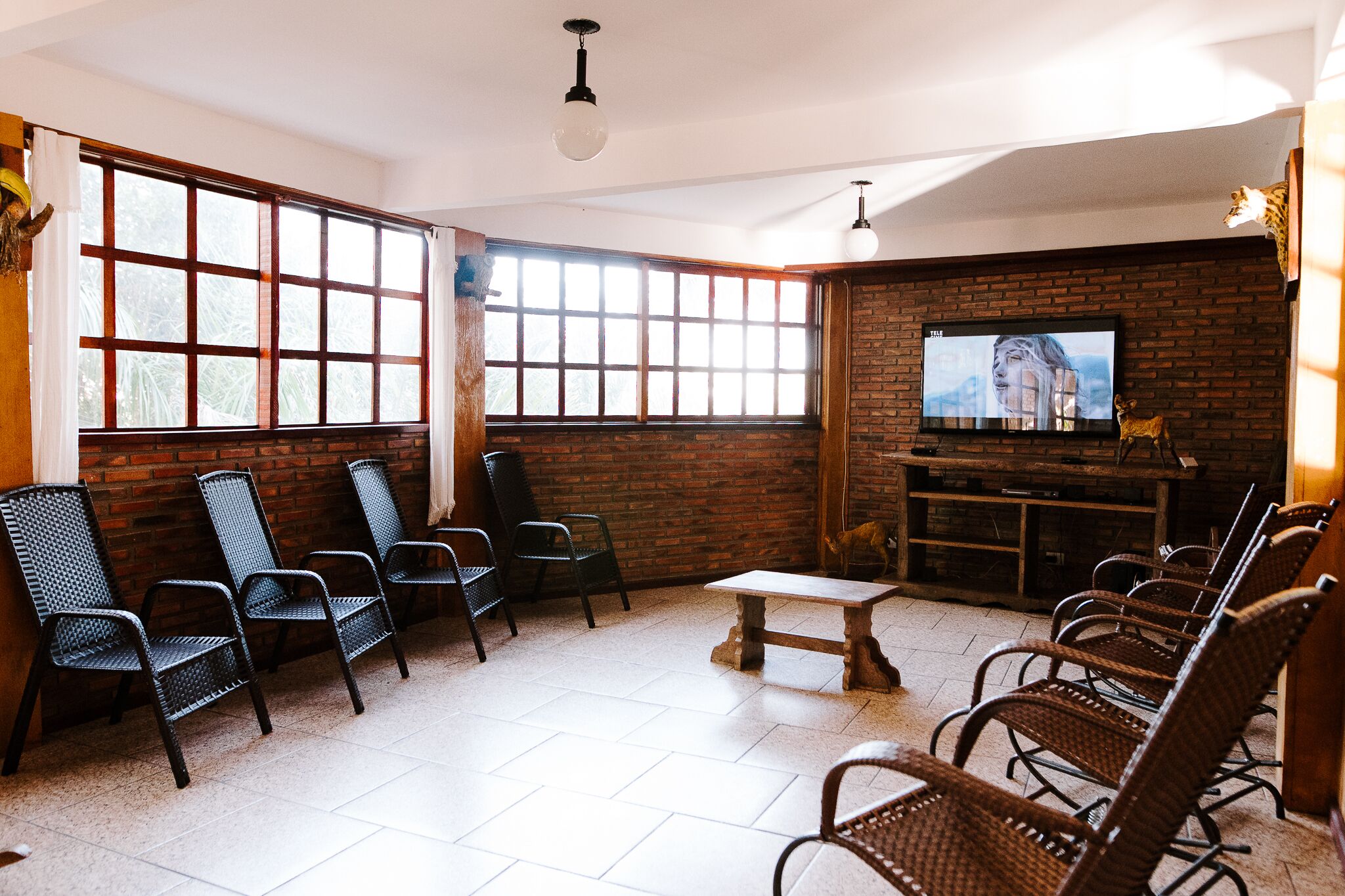A room with a brick wall, a television mounted on it, and several wicker chairs arranged around a small table.