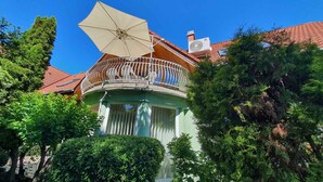 Un balcon d’angle agrémenté d’un parasol beige, d’un climatiseur blanc et d’un toit recouvert de tuiles rouges.
