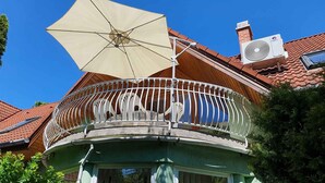 Un balcon avec un parasol blanc, un toit recouvert de tuiles rouges et un appareil de climatisation.
