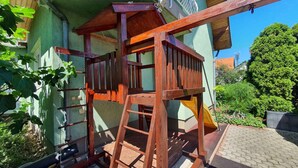 Une cabane en bois avec une échelle, adossée à un bâtiment vert doté d’un toit en tuiles.