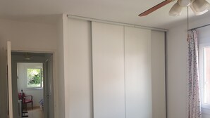 Een kamer met een schuifdeur, een plafondventilator en een raam met bloemen gordijnen.