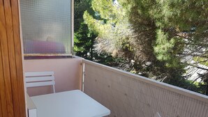 Een balkon met een witte tafel en stoelen, een houten deur en uitzicht op bomen.