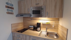 Una cocina compacta con armarios de madera, un lavamanos de acero inoxidable, un microondas, un tostador y una cafetera.
