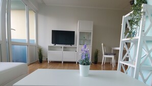 Una sala de estar moderna con un mueble blanco para entretenimiento, un televisor de pantalla plana, una mesa de centro blanca y una planta en maceta.
