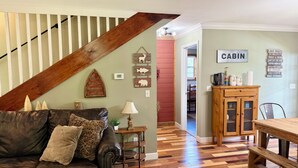 Una sala de estar con escalera de madera, un sofá de cuero, una mesa de comedor y una zona de cocina con un armario.