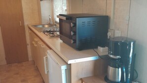 Et kompakt køkken med indbygget mikroovn, kaffemaskine og lille køleskab.