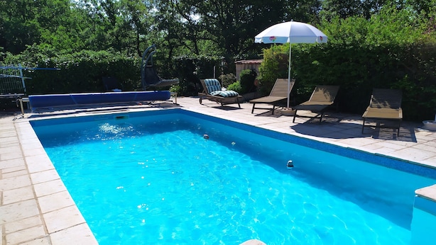 Et rektangulært pool med flisebelagt dæk, omgivet af liggestole og en parasol.