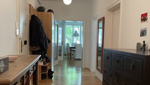Um corredor com piso de madeira, cozinha com bancada e armários de madeira, área de refeições com mesa e cadeiras, e um armário grande e escuro.