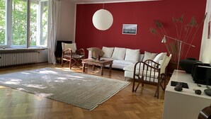 Uma sala de estar com parede vermelha, sofá branco, cadeiras de madeira, mesa de centro e uma grande janela.